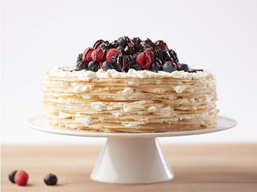 Berry crepe cake on a cake stand with berries on top